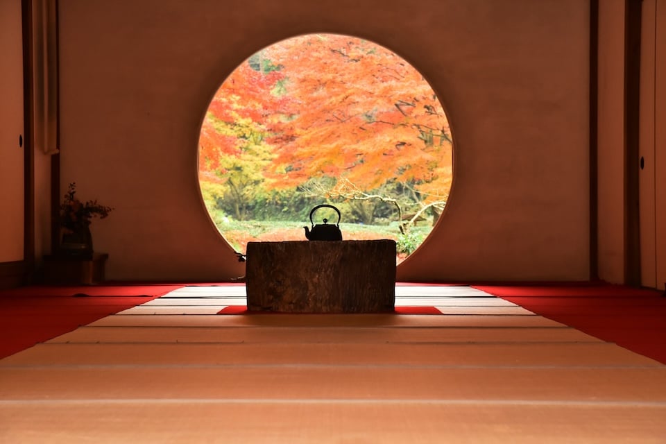 Autumn leaves viewed through a round window in a Japanese temple.