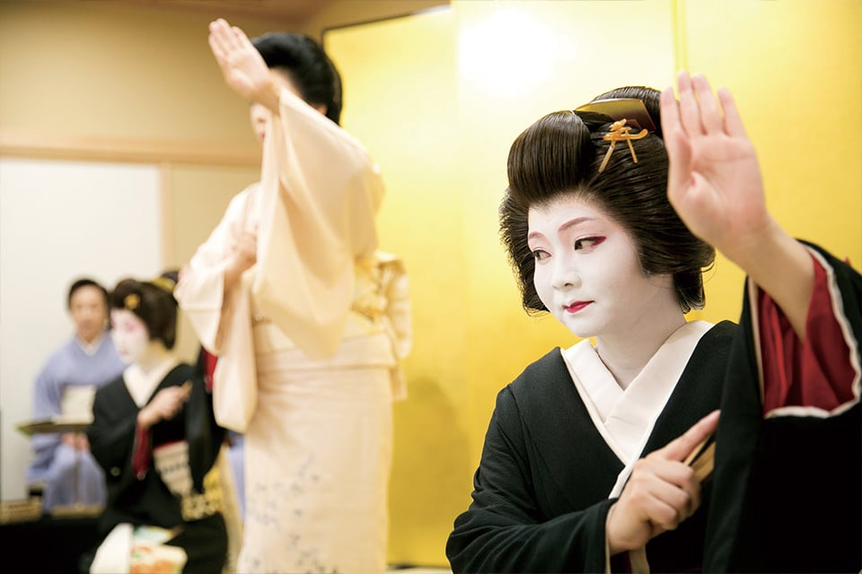 Geisha in a blue kimono interacting with a guest during a traditional dining experience at Asakusa Miyakodori in Tokyo